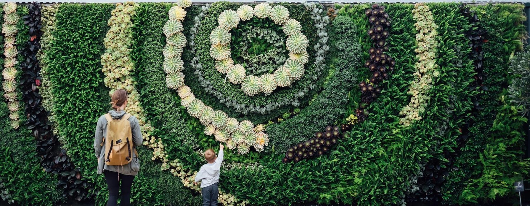mother and child standing in front of a mural made of plants